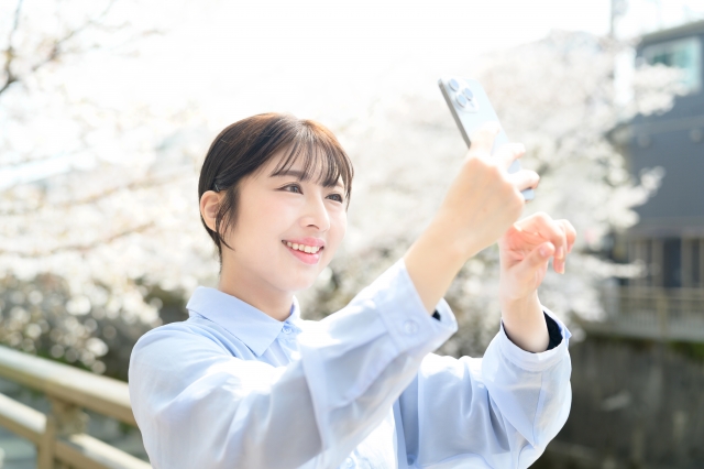 笑顔で桜を撮影する女性