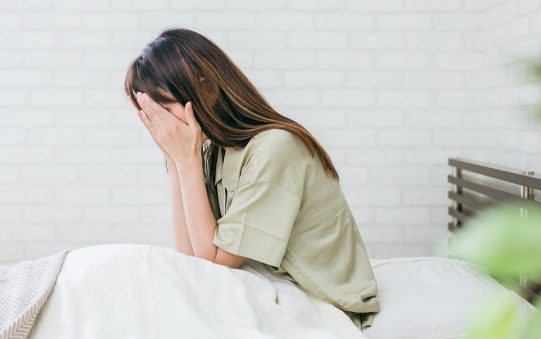 ベッドで顔を覆う女性